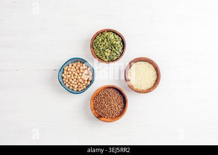 Cereals and seeds in bowls on white wooden table. Healthy food concept. Rice, chickpeas, buckwheat and pumpkin seeds. Top view, flat lay. Stock Photo