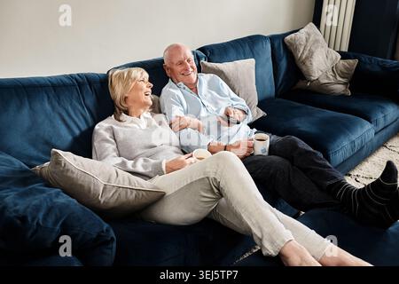 Coffee, watching tv and retirement with a senior couple on a sofa in the living room of their home for entertainment. Tea, smile or relax with a happy Stock Photo