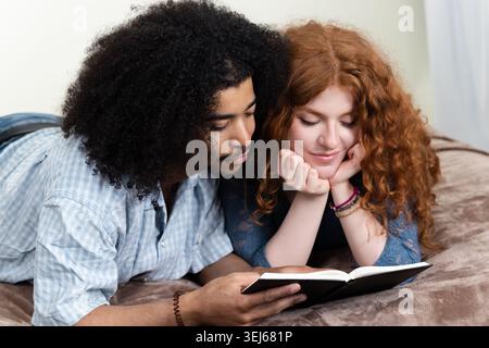 Interracial couple laying in bed reading a book, sharing a moment of intimacy and love Stock Photo