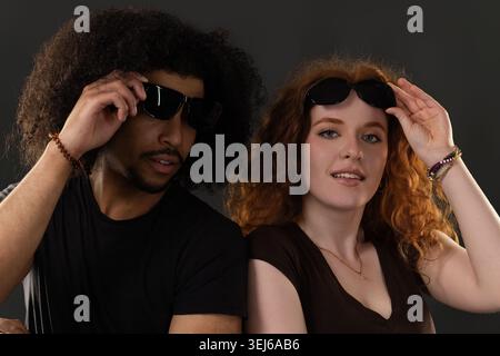 Interracial couple posing wearing sunglasses against gray background Stock Photo