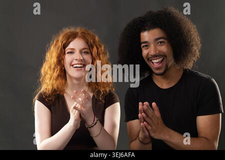 Cheerful multiracial couple clapping their hands, celebrating with big smiles Stock Photo