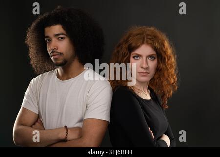 Young mixed race couple standing back to back with crossed arms, expressing tension and misunderstanding Stock Photo
