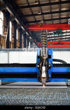 An optical fiber laser cutting machine is working in an industrial workshop. The main body of the equipment is blue-green, and the cutting head is pro Stock Photo