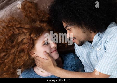 Young interracial couple lying down, showing affection and looking at each other Stock Photo