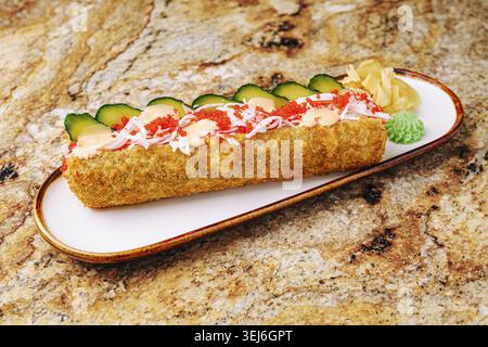 Food, A beautifully presented sushi roll is topped with vibrant fish roe, cucumber slices, and garnished with wasabi and pickled ginger. This dish sho Stock Photo