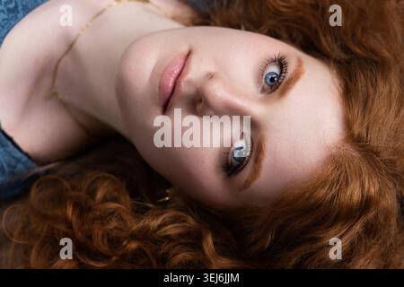 Young woman with beautiful red curly hair and striking blue eyes gazing directly Stock Photo