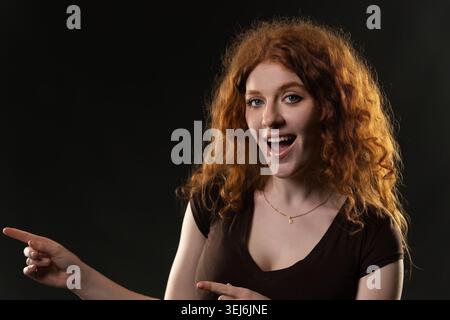 Redhead woman with curly hair pointing looking excited and surprised Stock Photo