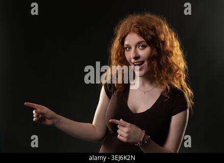 Redhead woman pointing left and down expressing surprise or excitement Stock Photo