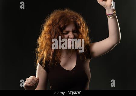 Young woman with curly red hair dancing actively, expressing strong emotion Stock Photo