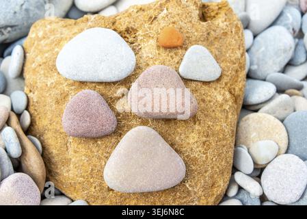 Triangular pebbles in varying colors artistically placed on a large, textured yellow rock, set against a pebble background Stock Photo