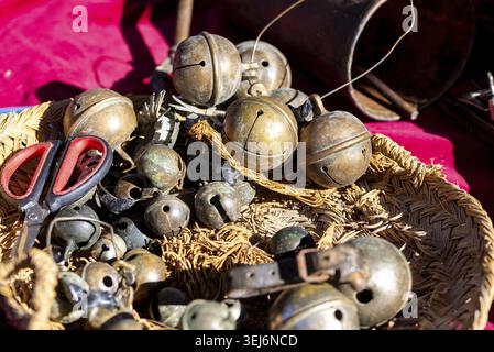 Close-up of old metal jingle bells in a woven wicker basket beside red handled scissors on bright pink cloth in warm sunlight outdoors Stock Photo