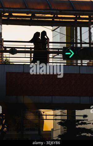 Balikpapan, Indonesia - May 21 2026. two women walking on a pedestrian overpass, moving in the same direction as a glowing green arrow signal of traffic. Stock Photo