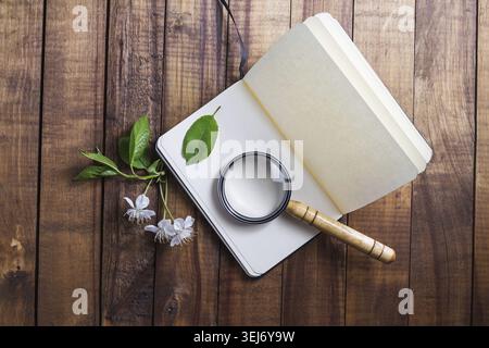 Photo of blank opened notebook, magnifier, cherry flowers and green leaves on vintage wooden table background. Stationery elements. Template for placi Stock Photo
