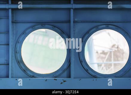 Two metal portholes with bolts on painted blue metal background. Inside view of the old aircraft Stock Photo