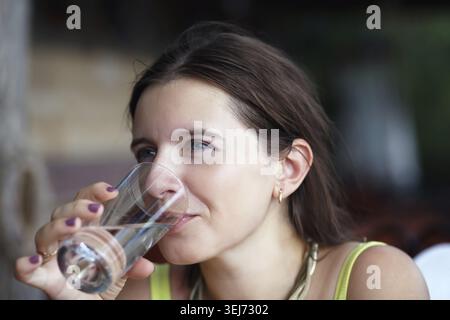 Pretty young woman drinking pure water from a transparent glass beaker. Selective focus Stock Photo