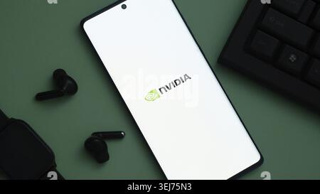 Dhaka, Bangladesh 23 May 2025:Nvidia logo on a smartphone placed on a green surface with nearby earbuds and a keyboard Stock Photo