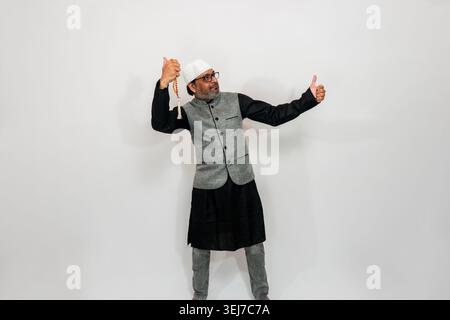 A man wearing traditional attire including a grey vest, black skirt/kilt, and a white cap with tassels. He is gesturing a thumbs up Stock Photo