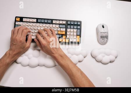 Top view of male hands typing on mechanical keyboard with custom keycaps and ergonomic cloud-shaped wrist rests, ensuring comfortable wrist support Stock Photo