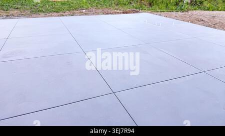 Smooth gray concrete surface with visible joints and a grassy area in the background Stock Photo