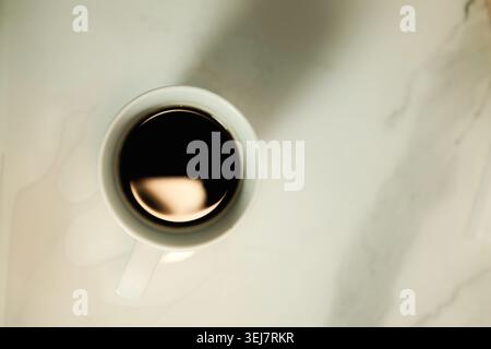 Elegant top view of dark coffee inside white ceramic mug with soft sunlight shadows. Minimal coffee aesthetic and calm lifestyle concept. Stock Photo