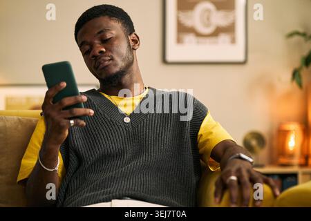 Young adult African American man checking smartphone while relaxing at home, expressing male friendship and digital connection. Ideal for social media, messaging, lifestyle marketing Stock Photo