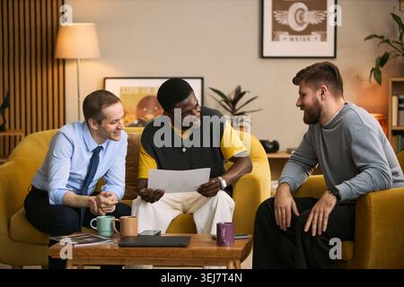 Multiethnic young adult men discussing document during casual meeting, expressing friendship and teamwork. Useful for campaigns about male bonding, community, support Stock Photo