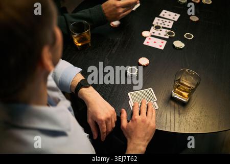 Young adult men playing poker, betting chips and holding cards around table, expressing male friendship and leisure bonding. Useful for nightlife, gambling, socializing marketing, top view Stock Photo