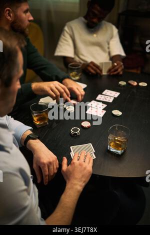 Vertical shot of young adult men playing poker, handling cards and chips around table, expressing male friendship and leisure bonding. Suitable for social lifestyle, gaming, mens community campaigns Stock Photo