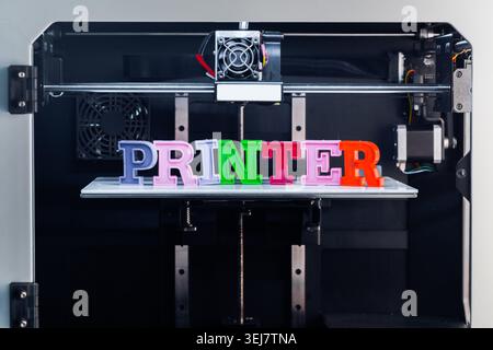 Colorful letters spelling printer sit on a 3D printing platform with machine in background Stock Photo