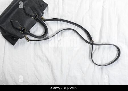 Black handbag placed on a soft white surface in a simple indoor setting Stock Photo