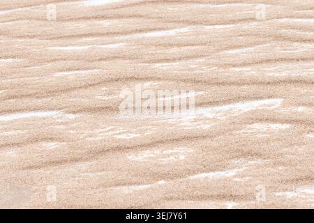 Soft, wind-sculpted sand ripples create a calm, minimal beach texture with warm beige tones and subtle white snowy streaks. Ideal as a background, pat Stock Photo