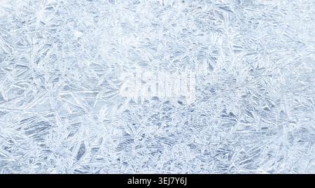 Close-up macro of a frozen ice surface revealing intricate frost crystals and geometric patterns in cool blue tones, delicate texture ideal for winter Stock Photo