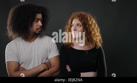 Interracial couple standing with crossed arms, looking away, symbolizing tension and emotional distance Stock Photo