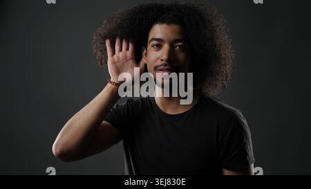 Young man with curly hair paying close attention, cupping hand to ear Stock Photo