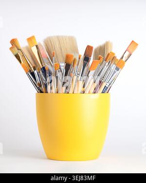 Artist paint brushes in a yellow flower pot. Mix of new and used artist brushes, in various sizes and widths. Stock Photo