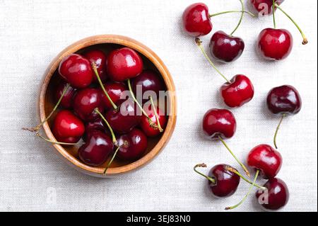 Fresh cherries in a wooden bowl on linen. Ready to eat, red and ripe fruits of the true cherry species Prunus avium, a stone fruit cultivar. Stock Photo