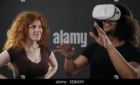 Couple engaging with VR technology, one experiencing a virtual world while other observing Stock Photo