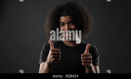 Young man with afro hair giving two thumbs up, expressing approval Stock Photo