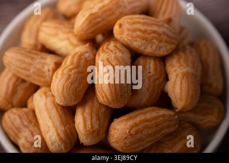 close-up view of a bowl filled with golden-brown mini choux pastries and eclairs, highlighting ridged striped textures, warm tones, shallow depth-of-f Stock Photo
