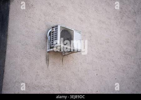 worn white outdoor air-conditioning unit mounted on a textured beige stucco wall, showing rust, grime and mildew stains, minimal urban decay compositi Stock Photo