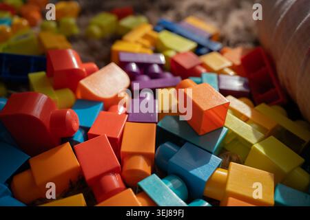 close-up of colorful interlocking plastic building blocks scattered across a soft rug, warm natural sunlight illuminating vibrant reds, oranges, blues Stock Photo