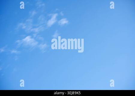 clear bright blue sky with delicate wispy clouds clustered in the upper-left, minimalist open composition conveying serene, airy midday light, soft gr Stock Photo