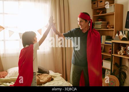 Father and Son Giving High Five during Imaginative Play at Home Stock Photo