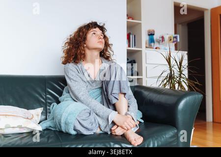 young red-haired woman relaxing on leather sofa Stock Photo