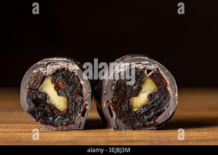 Macro shot of two chocolate candies cut in half showing prune and walnut filling inside. Gourmet handmade sweets on wooden background. Chocolate cover Stock Photo