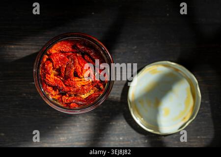 Gourmet sun dried tomatoes in oil inside a glass jar on dark background, close up. Top view of traditional Mediterranean food appetizer with moody lig Stock Photo