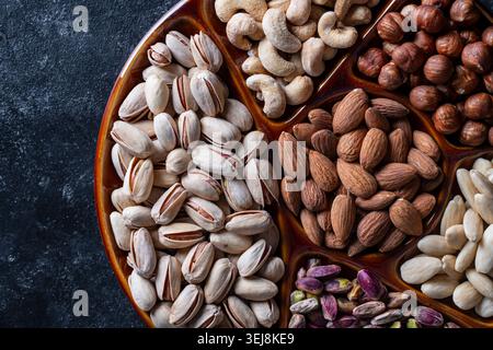 Assorted nuts platter background overhead close up. Top view of mixed nuts including pistachios, almonds, cashews, and hazelnuts in a ceramic serving Stock Photo