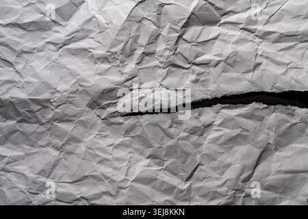 Texture of crumpled white paper with a horizontal ripped torn edge opening showing a dark black contrast background, top view Stock Photo