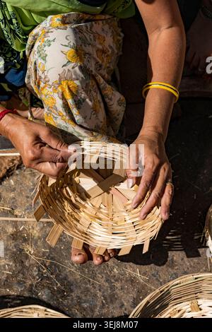 Indian woman weaving a traditional bamboo basket by hand. Close up high angle view of an artisan female hands carefully weaving a handmade bamboo stra Stock Photo