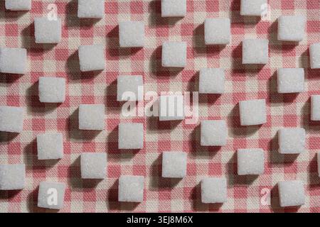 White sugar cubes pattern on pink checkered tablecloth top view. Geometric flat lay pattern of refined white sugar cubes with hard shadows on a pink p Stock Photo